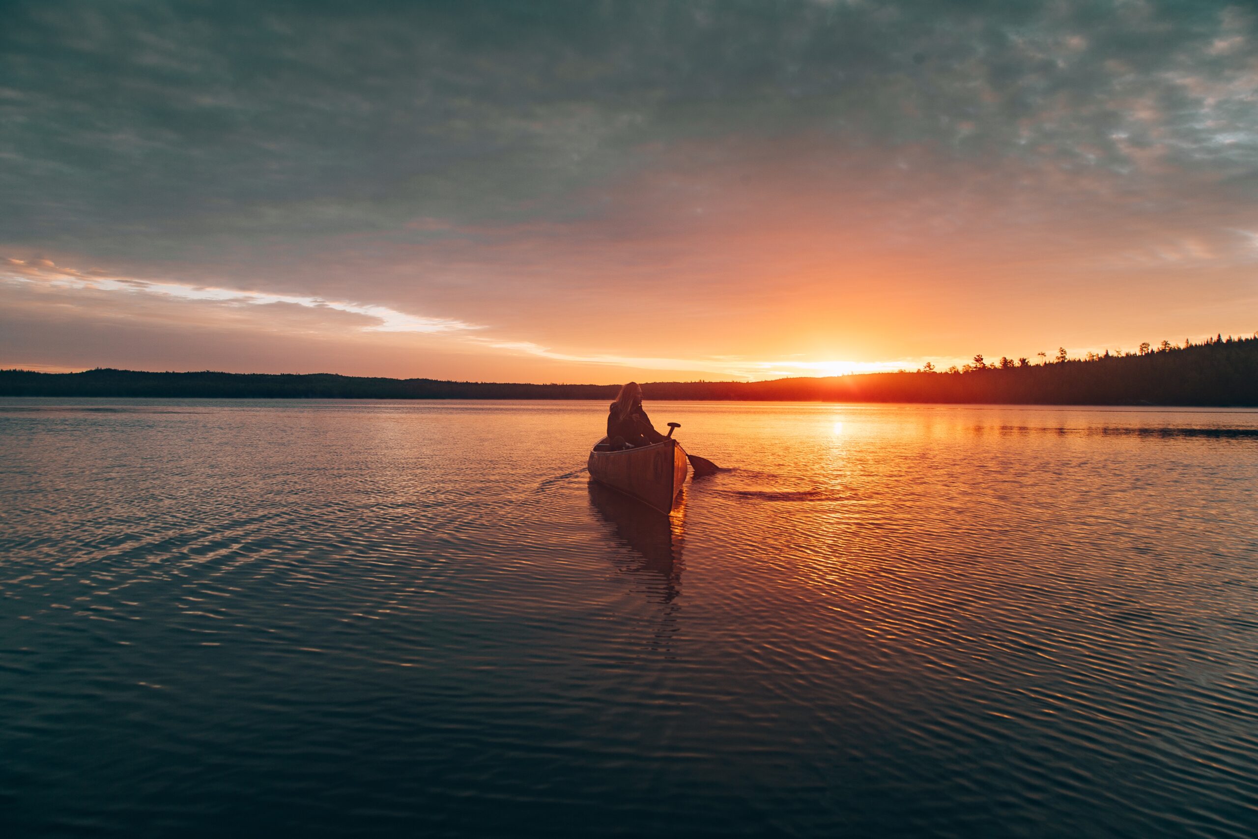 A beautiful distant shot of a female riding  kayak in the middle of a lake during sunset